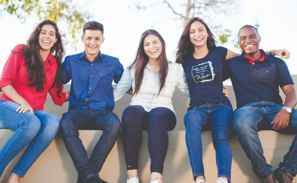 Group of five young adults sitting outside on a bench smiling, representing youth career services at Workforce Solutions Capital Area